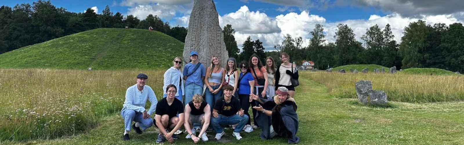 Program participants and leaders posing in a grassy field, in front of a large stone relic with markings on it.